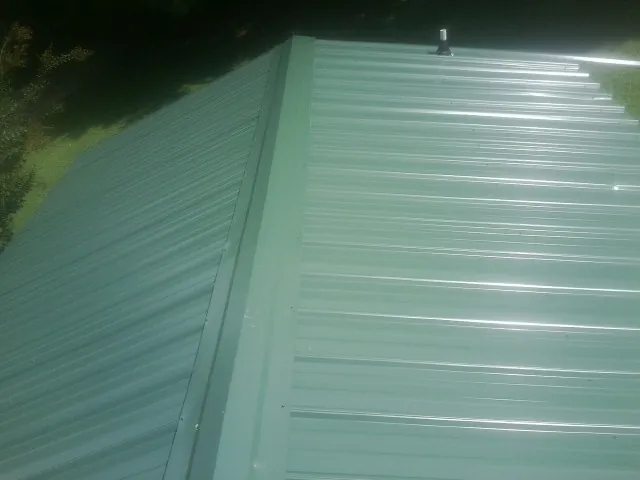 New green metal panels meeting at the ridge of a roof — Flat Roof Repair work by our crew in Temperanceville