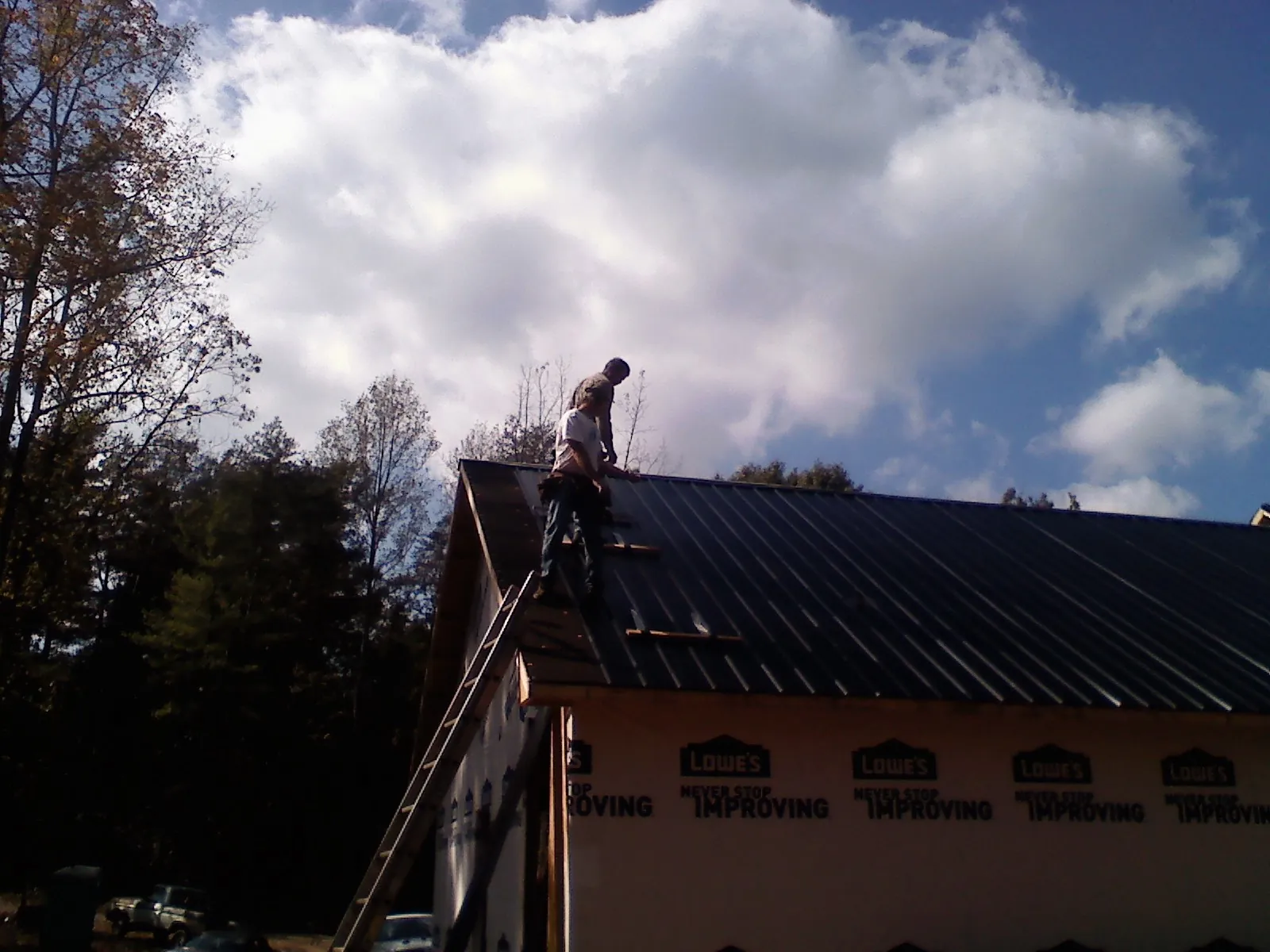 Roofer fastening dark metal panels high against a cloudy sky, from a Roof Inspection job in Temperanceville
